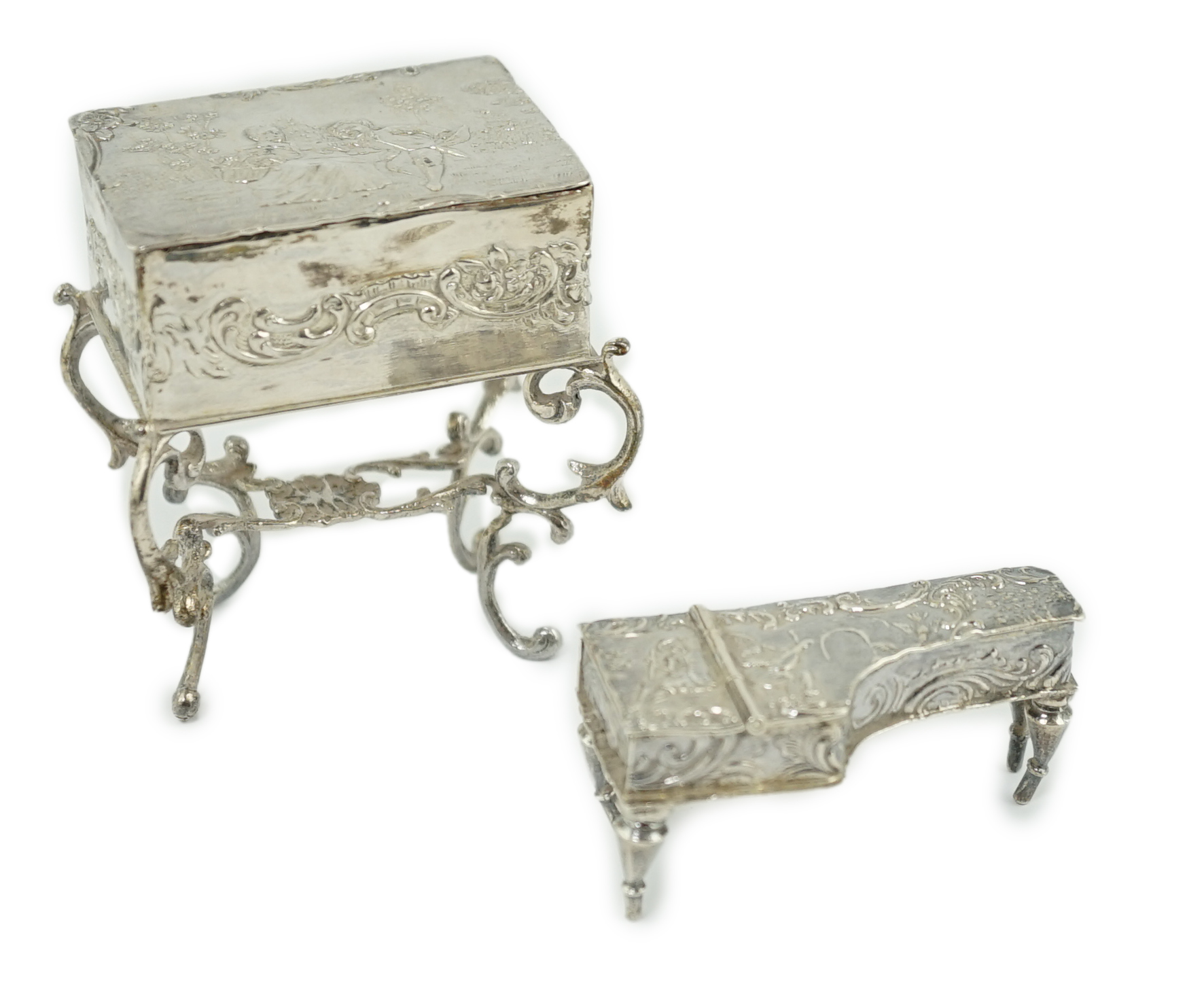 A late 19th century continental embossed silver miniature model of grand piano, length 53mm, together with a similar model of a table/desk on ornate scroll supports